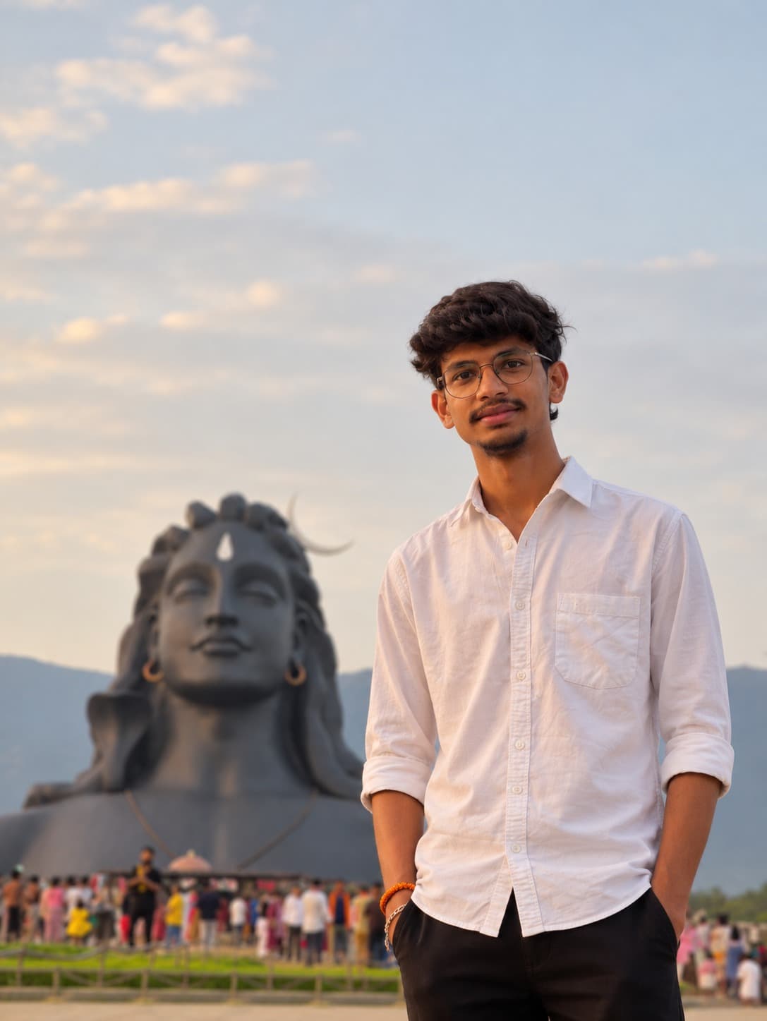 Sunil outdoors in a white shirt, smiling, with a large statue and hills behind him